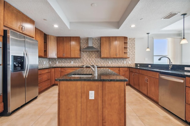 kitchen featuring appliances with stainless steel finishes, pendant lighting, an island with sink, sink, and wall chimney range hood