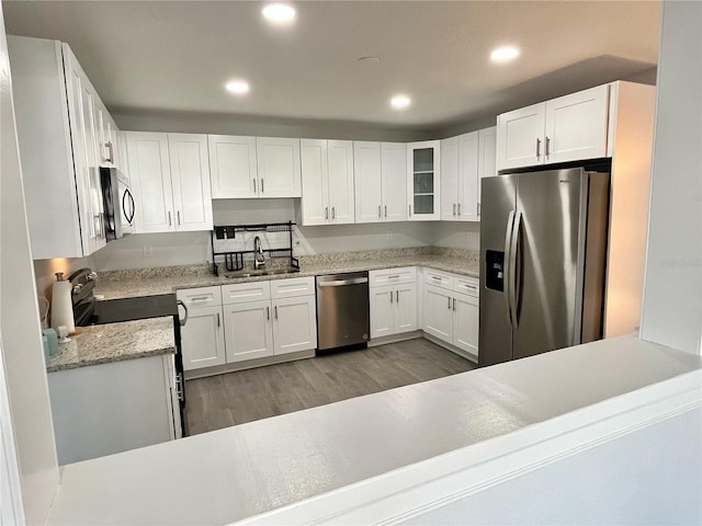 kitchen with white cabinetry, appliances with stainless steel finishes, dark wood-type flooring, light stone countertops, and sink