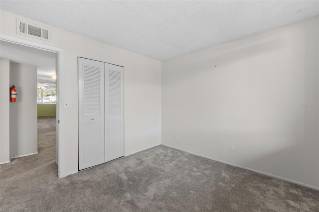 unfurnished bedroom with a textured ceiling, carpet floors, a closet, and visible vents