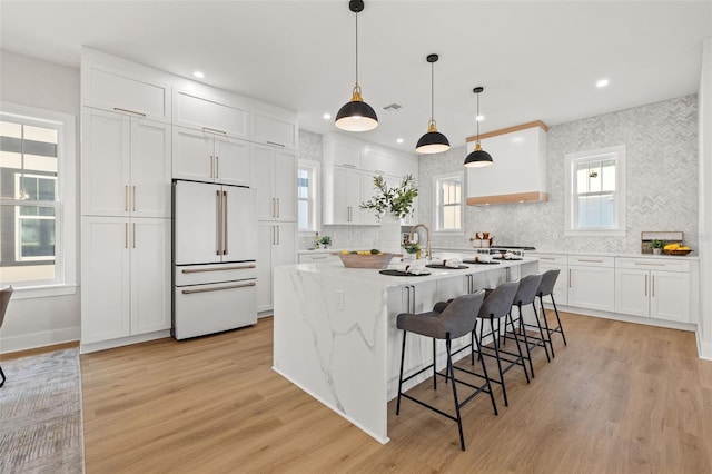 kitchen with white cabinetry, hanging light fixtures, high end white fridge, and light wood-type flooring