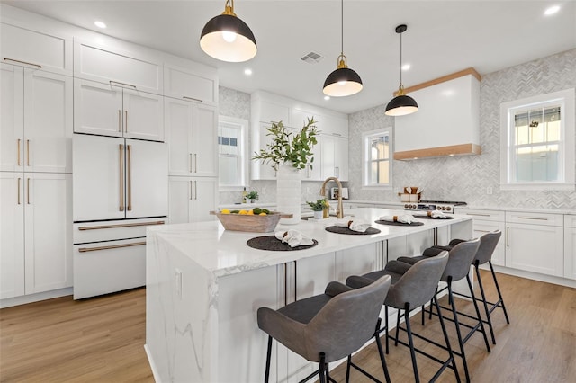 kitchen with hanging light fixtures, white cabinets, built in refrigerator, a kitchen island with sink, and a kitchen bar