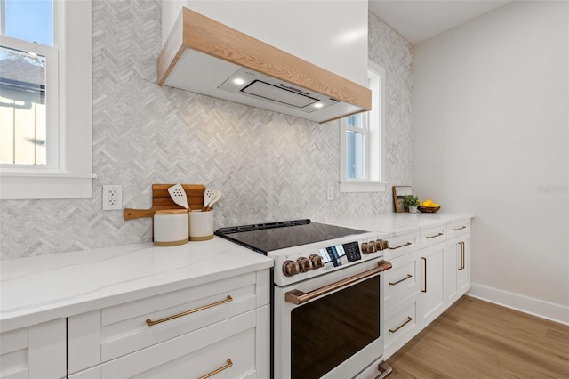 kitchen featuring custom exhaust hood, white cabinetry, stainless steel electric range, light stone counters, and plenty of natural light