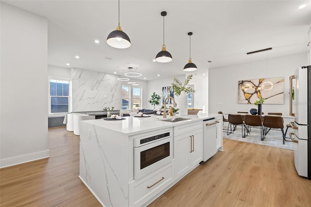 kitchen featuring white appliances, white cabinets, decorative light fixtures, sink, and a kitchen island with sink