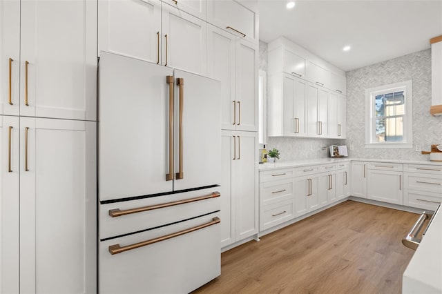 kitchen featuring white cabinets, tasteful backsplash, high end fridge, and light wood-type flooring