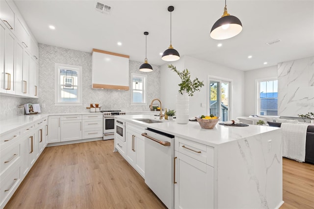 kitchen featuring white appliances, a kitchen island with sink, white cabinets, sink, and pendant lighting