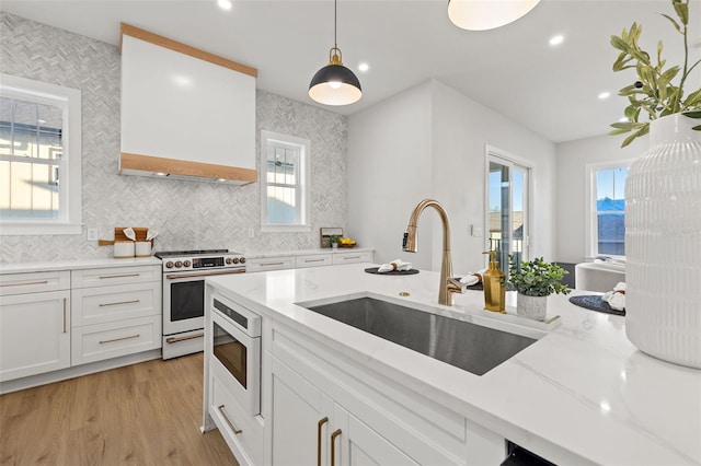 kitchen with light stone countertops, white cabinets, high end white range, sink, and hanging light fixtures