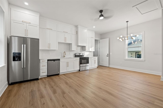 kitchen featuring appliances with stainless steel finishes, decorative light fixtures, white cabinetry, sink, and light hardwood / wood-style flooring