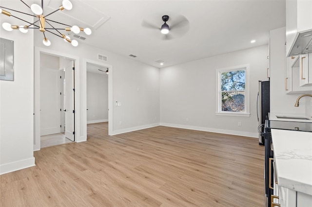 unfurnished dining area featuring sink, ceiling fan with notable chandelier, and light hardwood / wood-style flooring