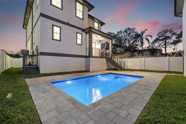 pool at dusk with a patio and a lawn