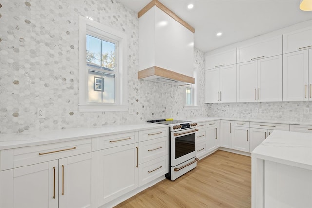 kitchen featuring premium range hood, white cabinets, electric range, light hardwood / wood-style floors, and light stone counters