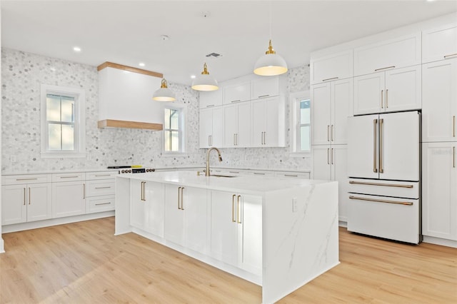 kitchen with high end white fridge, sink, a center island with sink, white cabinets, and hanging light fixtures