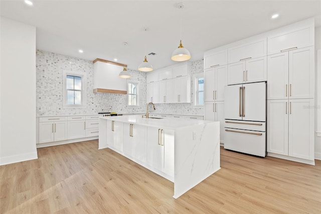 kitchen with high end white refrigerator, white cabinetry, pendant lighting, and light wood-type flooring