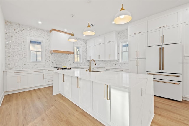 kitchen featuring white cabinets, sink, high end white fridge, an island with sink, and decorative light fixtures