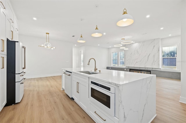 kitchen featuring refrigerator, white dishwasher, sink, decorative light fixtures, and a center island with sink