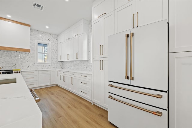 kitchen featuring light stone countertops, decorative backsplash, high end fridge, white cabinets, and light wood-type flooring