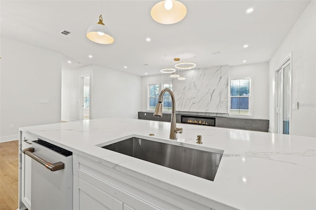 kitchen featuring light stone countertops, dishwasher, sink, plenty of natural light, and pendant lighting