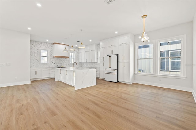 kitchen with high end white refrigerator, light hardwood / wood-style flooring, white cabinets, and decorative light fixtures