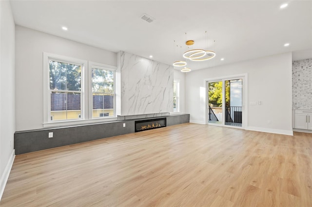 unfurnished living room featuring a fireplace, a healthy amount of sunlight, a notable chandelier, and light wood-type flooring