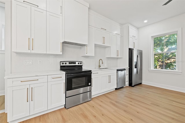 kitchen with white cabinets, sink, light wood-type flooring, appliances with stainless steel finishes, and light stone counters