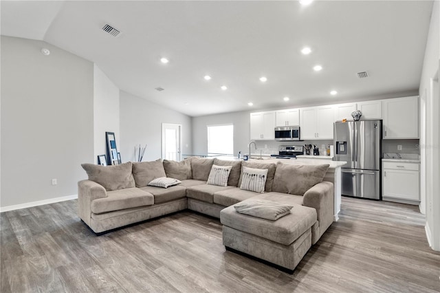 living room featuring lofted ceiling, sink, and light wood-type flooring