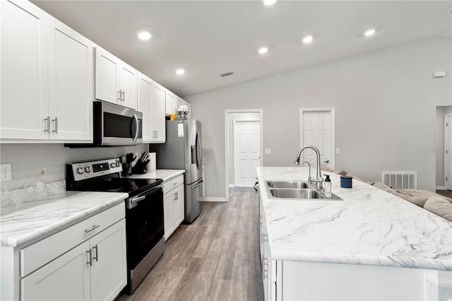 kitchen with sink, appliances with stainless steel finishes, an island with sink, white cabinets, and vaulted ceiling