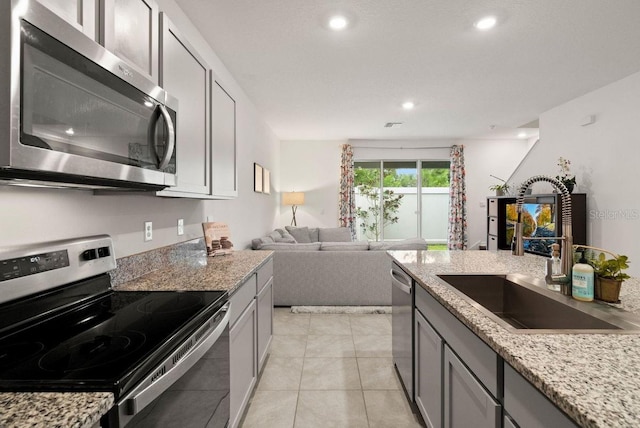 kitchen with appliances with stainless steel finishes, sink, light stone countertops, gray cabinets, and light tile patterned flooring