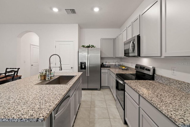 kitchen with light stone countertops, appliances with stainless steel finishes, a kitchen island with sink, gray cabinetry, and sink