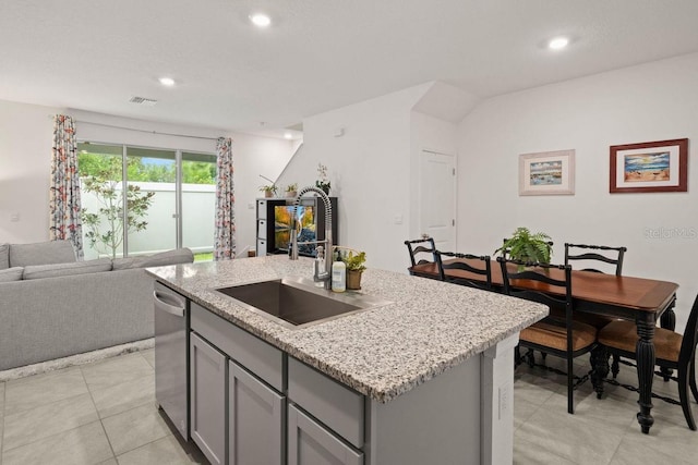 kitchen featuring dishwasher, a kitchen island with sink, gray cabinetry, sink, and light stone counters