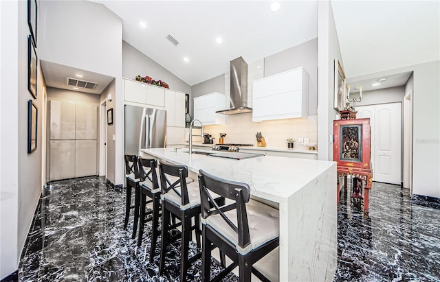 kitchen with white cabinetry, sink, wall chimney range hood, light stone counters, and a breakfast bar