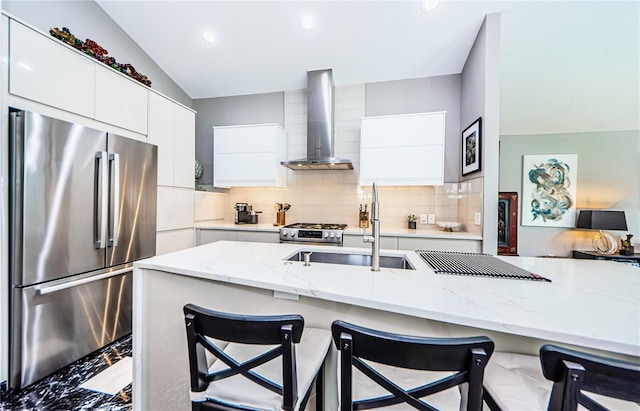 kitchen featuring appliances with stainless steel finishes, light stone counters, wall chimney exhaust hood, and a breakfast bar area