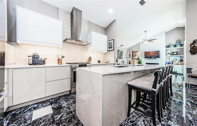 kitchen with stainless steel range, ceiling fan, wall chimney range hood, white cabinetry, and lofted ceiling