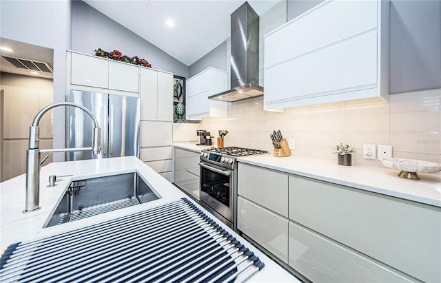 kitchen featuring white cabinetry, stainless steel appliances, wall chimney range hood, vaulted ceiling, and decorative backsplash