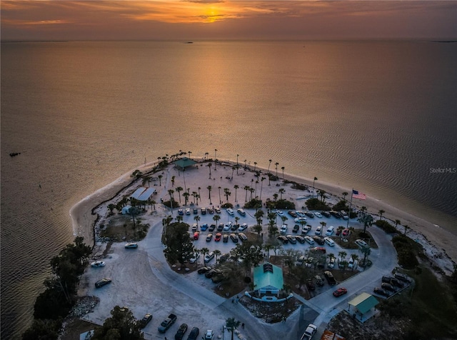 aerial view at dusk featuring a water view and a view of the beach