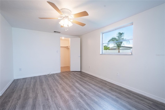 unfurnished bedroom featuring hardwood / wood-style floors, a closet, a spacious closet, and ceiling fan