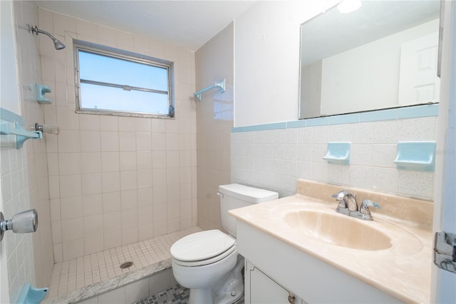 bathroom with tiled shower, vanity, toilet, and tile walls