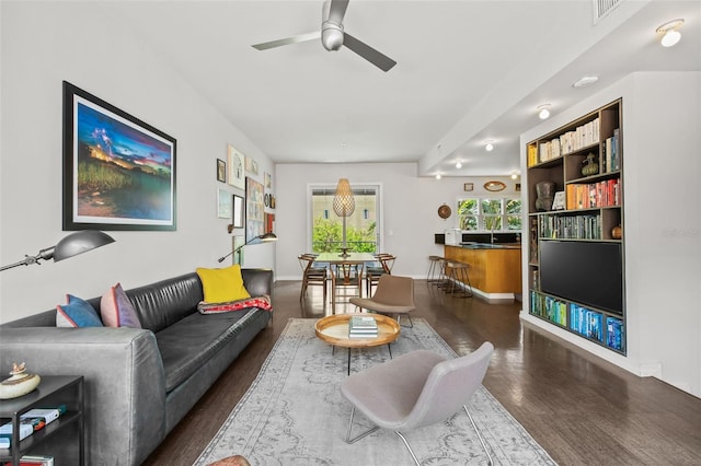 living room with built in shelves, dark wood-type flooring, and ceiling fan