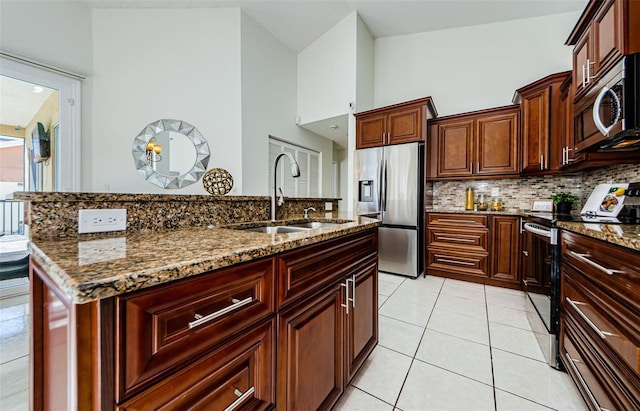 kitchen featuring light tile patterned floors, a center island with sink, stainless steel appliances, dark stone countertops, and sink