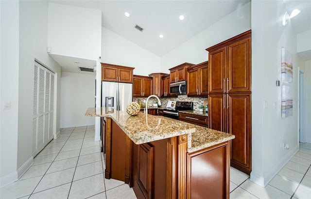 kitchen with an island with sink, stainless steel appliances, decorative backsplash, high vaulted ceiling, and light stone countertops