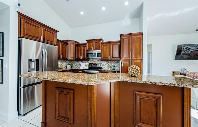 kitchen with lofted ceiling, backsplash, a spacious island, light tile patterned flooring, and appliances with stainless steel finishes