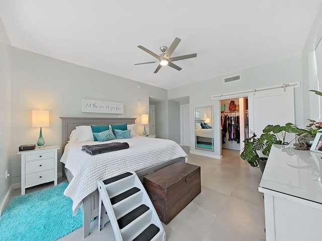 bedroom with a walk in closet, a closet, ceiling fan, and a barn door