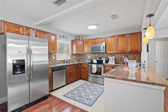 kitchen featuring tasteful backsplash, pendant lighting, light wood-type flooring, appliances with stainless steel finishes, and kitchen peninsula