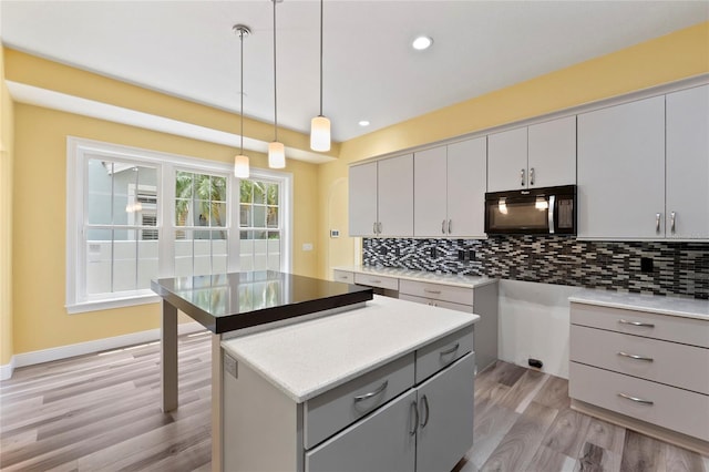 kitchen featuring gray cabinetry, decorative backsplash, hanging light fixtures, a center island, and light hardwood / wood-style flooring