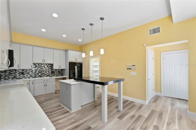 kitchen featuring black fridge with ice dispenser, white cabinetry, tasteful backsplash, decorative light fixtures, and a center island