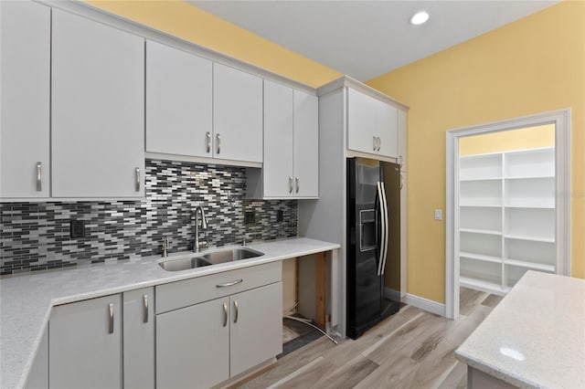 kitchen featuring sink, white cabinetry, tasteful backsplash, light hardwood / wood-style floors, and black refrigerator with ice dispenser