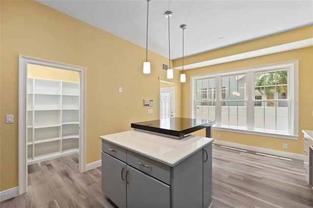 kitchen featuring a kitchen island, pendant lighting, gray cabinetry, light stone countertops, and light wood-type flooring