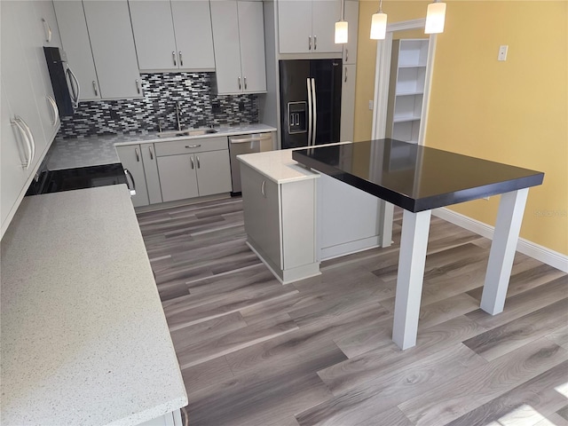 kitchen featuring light wood finished floors, a sink, stainless steel appliances, decorative light fixtures, and backsplash