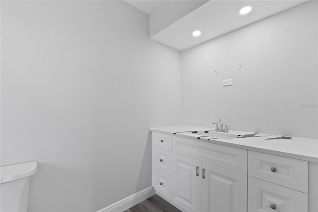 half bathroom featuring vanity, wood finished floors, baseboards, recessed lighting, and toilet