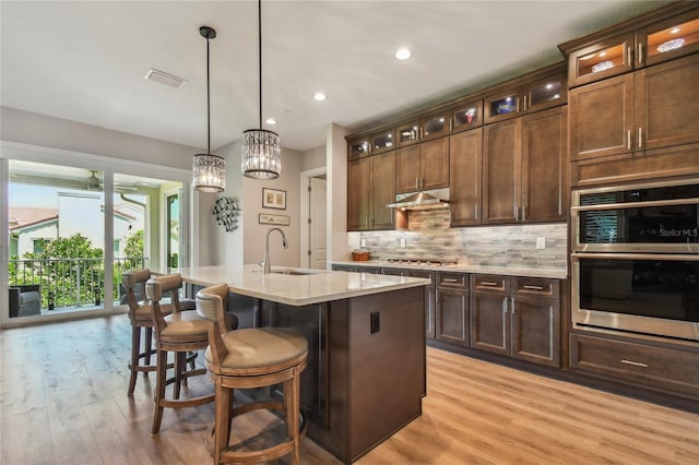 kitchen featuring sink, stainless steel appliances, dark brown cabinetry, an island with sink, and decorative light fixtures