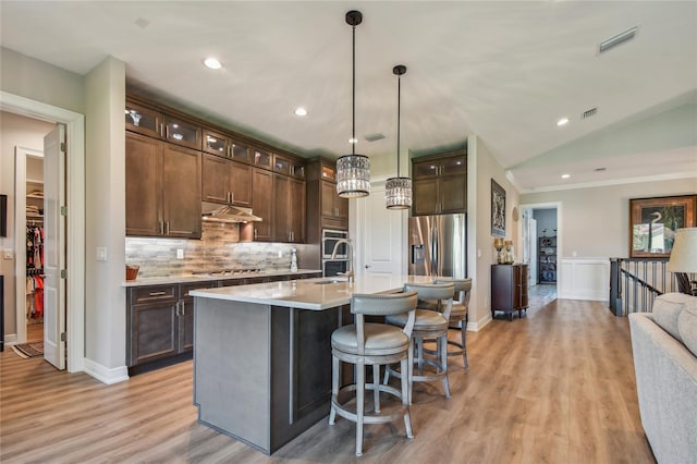 kitchen with hanging light fixtures, vaulted ceiling, appliances with stainless steel finishes, and dark brown cabinetry