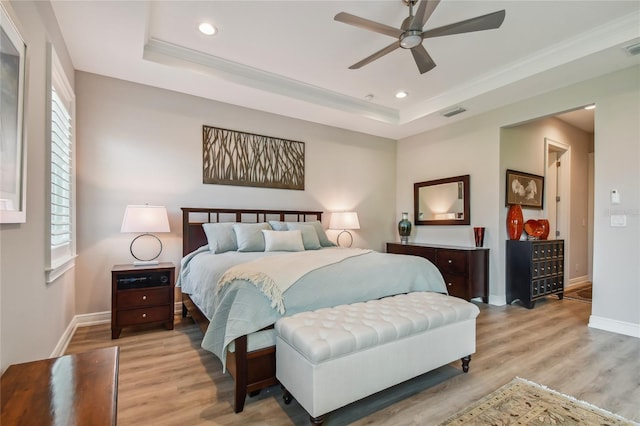 bedroom featuring light hardwood / wood-style flooring, ornamental molding, a raised ceiling, and ceiling fan